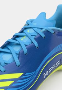 Blue athletic shoe featuring a sleek design, synthetic material, prominent yellow accents, and textured laces. "MESSI" logo displayed on the side.