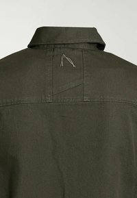 Collet en tissu vert foncé avec une couture cousue et une petite lettre brodée "A" sur le haut du dos du vêtement.