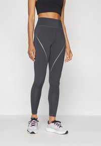 Leggings a vita alta, aderenti, di colore grigio scuro con accenti di cucitura in grigio chiaro a contrasto. Abbinati a scarpe da ginnastica bianche e rosa.