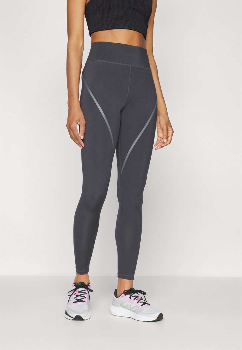 Leggings a vita alta, aderenti, di colore grigio scuro con accenti di cucitura in grigio chiaro a contrasto. Abbinati a scarpe da ginnastica bianche e rosa.