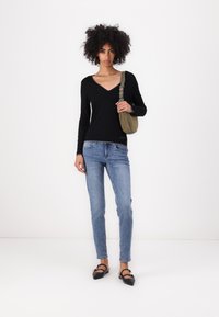 Maglietta nera a maniche lunghe con scollo a V, jeans blu slim-fit, ballerine nere e una piccola borsa a tracolla verde oliva. Design semplice e colori neutri.