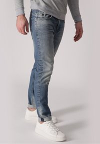 Džíny z denimu ve světle modré barvě se střihovým zakončením rovnými nohavicemi, s jemným opotřebením a ohrnutými manžetami. V kombinaci s bílými teniskami.