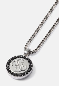 Colar de metal com um pendant circular, apresentando um logotipo prateado rodeado por pedras negras. A corrente tem um design torcido.