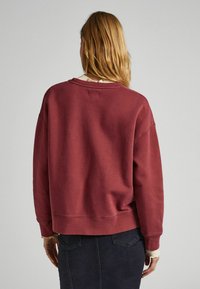 Felpa oversized color bordeaux con scollatura tonda e spalle scese. Materiale in cotone morbido con polsini e orlo in costina. Design semplice, senza fantasie.