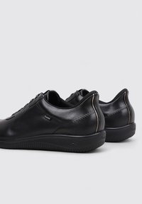 Par de zapatillas de cuero negro de corte bajo con suelas redondeadas y sutiles detalles de costura sobre un fondo claro y liso.