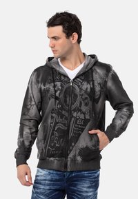 Haut de sweat à capuche zippé noir et gris avec une impression graphique aux motifs vintage, une capuche avec cordon de serrage et deux poches avant.