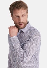 Weißes Hemd mit einem kleinen, feinen geometrischen Muster in Blau und Rot, langen Ärmeln, Schalkragen und blauen Knöpfen an den Manschetten und dem Knopfbereich.