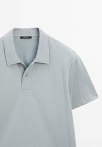 Lys grå kortærmet polo skjorte med krave og enkelt knaplukning, præsenteret på en hvid baggrund.