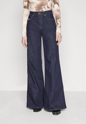 Personne portant un jean bleu foncé taille haute à jambes larges, associé à un haut ajusté à manches longues et des chaussures noires à bout carré.