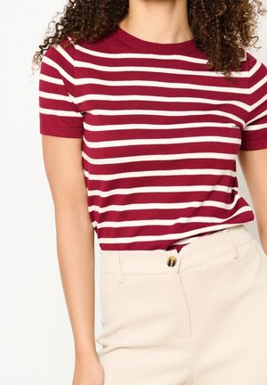 Top de manga corta a rayas rojas y blancas con cuello redondo acanalado, combinado con pantalones de tiro alto beige con textura que cuentan con un detalle de botón dorado.
