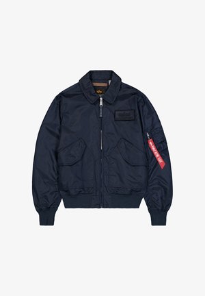 Granatowa kurtka bombowiec z przednimi kieszeniami na klapki, ściągaczami przy mankietach i dolnym brzegu, zamkiem błyskawicznym oraz czerwoną metką "Remove Before Flight" na kieszeni lewego rękawa.