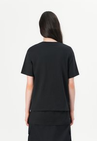 Černé bavlněné tričko s krátkým rukávem a kulatým výstřihem. Má volný střih, hladkou strukturu a minimalistický design.