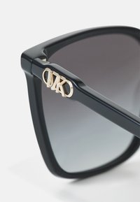 Black acetate sunglasses with a square shape, gradient gray lenses, and a gold MK logo accent on the temple. Smooth, glossy finish.