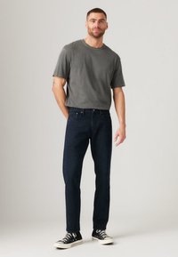 Dark blue denim jeans paired with a gray crew-neck t-shirt and black sneakers. The outfit features a relaxed fit and minimal detailing.