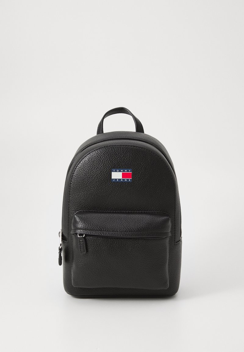 Schwarzer Leder-Rucksack mit runder Form, strukturiertem Bezug, vorderer Reißverschlusstasche und einem Logopatch in den Farben Rot, Weiß und Blau.