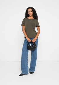 Olive green short-sleeve t-shirt with a textured pocket, paired with high-waisted blue jeans and a black leather handbag.
