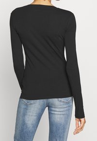 Maglietta nera a maniche lunghe con un design aderente, caratterizzata da un collo a giro e una texture liscia, abbinata a jeans azzurri chiari.