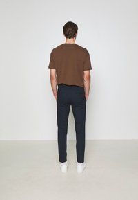 T-shirt marron à manches courtes et pantalon slim-fit bleu marine, accompagné de baskets blanches. Le t-shirt a un col rond et des manches retroussées.