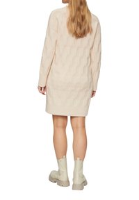 Beige gestricktes Sweaterkleid mit einem strukturierten sechseckigen Muster, langen Ärmeln und geripptem Saum, kombiniert mit weißen Knöchelboots.