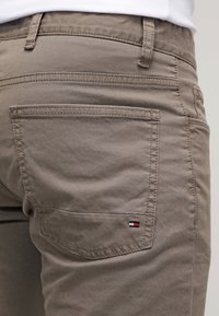 Grijze katoenen chino's met een achterzak en een klein geborduurd logo in rood, wit en blauw. Gladde textuur en rechte pasvorm.