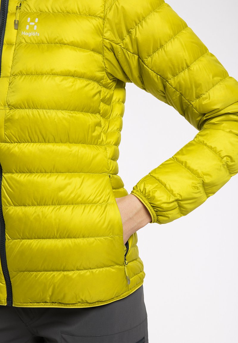 Grüne Daunenjacke mit horizontalen Nähten, ausgestattet mit einer Reißverschlusstasche und elastischen Bündchen. Leichtes, wasserabweisendes Material.