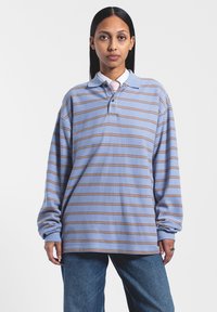 Gestreepte langärmige polo-shirt in lichtblauw met tan strepen, met een klassieke kraag, twee knopen en een relaxte pasvorm. Blauwe jeans getoond.