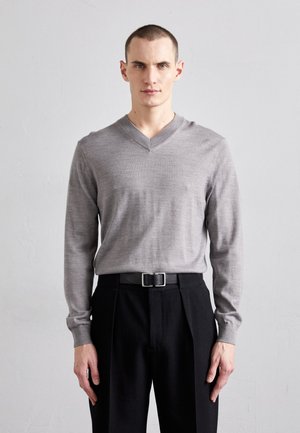 Grau V-Ausschnitt Pullover mit langen Ärmeln, weicher Textur; kombiniert mit hochgeschnittenen schwarzen Hosen, die einen Gürtel und eine rechteckige silberne Schnalle haben.