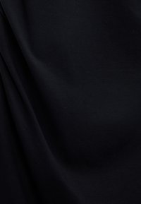 Schwarzer Stretchstoff mit glatter Textur, der subtile Falten und Variationen in Licht und Schatten aufweist. Weicher und opaker Eindruck.