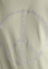 Světle zelená látka s velkým symbolem míru vyrobeným ze stříbrných kamínků, s hladkou texturou a kulatým designem s jemnými detaily.