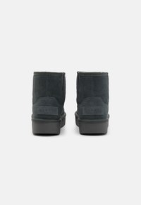 Stivaletti alla caviglia in suede grigio scuro con punta arrotondata, suola in gomma piatta e logo discreto sul retro. Presentano una superficie liscia e cuciture minime.