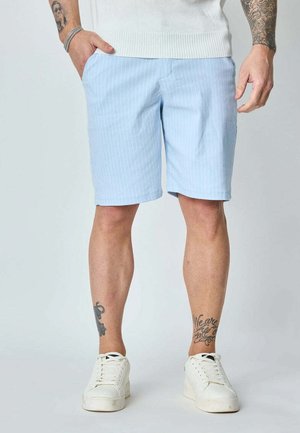 Shorts bleu clair à rayures faites d'un tissu, avec des poches latérales, une coupe droite et une taille simple, associés à des baskets blanches.