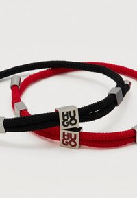 Kaksi punottua rannekorua, yksi musta ja yksi punainen, molemmissa metalliset neliökoristeet, joissa "HUGO"-brändäys. Valmistettu teksturoidusta köysimateriaalista.