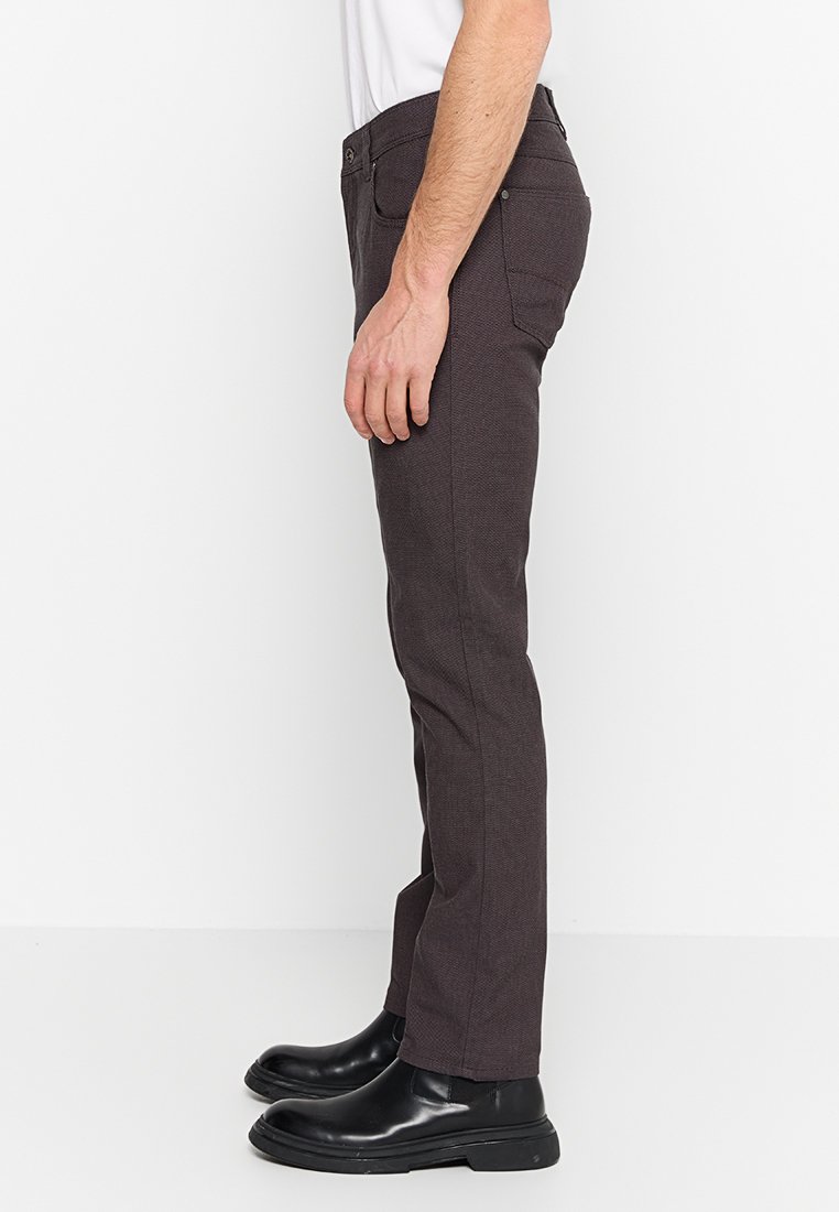 Dunkelbraune Slim-Fit-Hosen aus strukturiertem Stoff mit einem klassischen Fünf-Taschen-Design, getragen mit schwarzen Leder-Ankle-Boots.