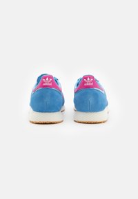 Blue suede sneakers with a pink heel accent. Features textured outsole and Adidas branding on the heel.