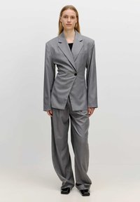 Grijze op maat gemaakte pak met een oversized blazer met een enkele knoop, wijde pijpen en een zachte textuur. Draag het over een zwarte top.