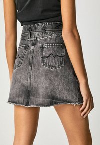 Svart denimmini kjol med fransad nederkant, bakfickor med vågmönsterstygning och bältesöglor. Strukturerad tyg och figurnära design.