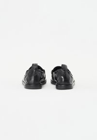 Zwarte leren instapschoenen met een gestructureerde bovenkant, elastisch ontwerp en een klein logo op de hiel. Gladde zool met minimale profiel.