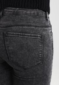 Jeans de denim negro con un ajuste slim, detalles en el bolsillo trasero y una tela texturizada con sutiles efectos de desvanecimiento.