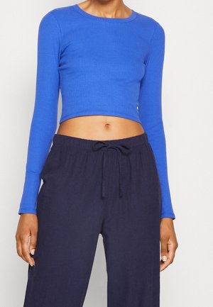 Sininen ribattu pitkähihainen crop-top, joka on yhdistetty tummansinisiin nyörillisiin housuihin. Topissa on pyöreä kaula-aukko ja se on vartalonmyötäinen.