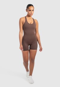 Brun ärmlös bodysuit med en åtsittande design och stretchigt tyg, i kombination med vita sportskor, mot en neutral bakgrund.