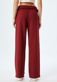 Bredde bukser i burgundy stof med en elastisk, flæset talje og frynset kantdetaljer. Glat tekstur, afslappet design.