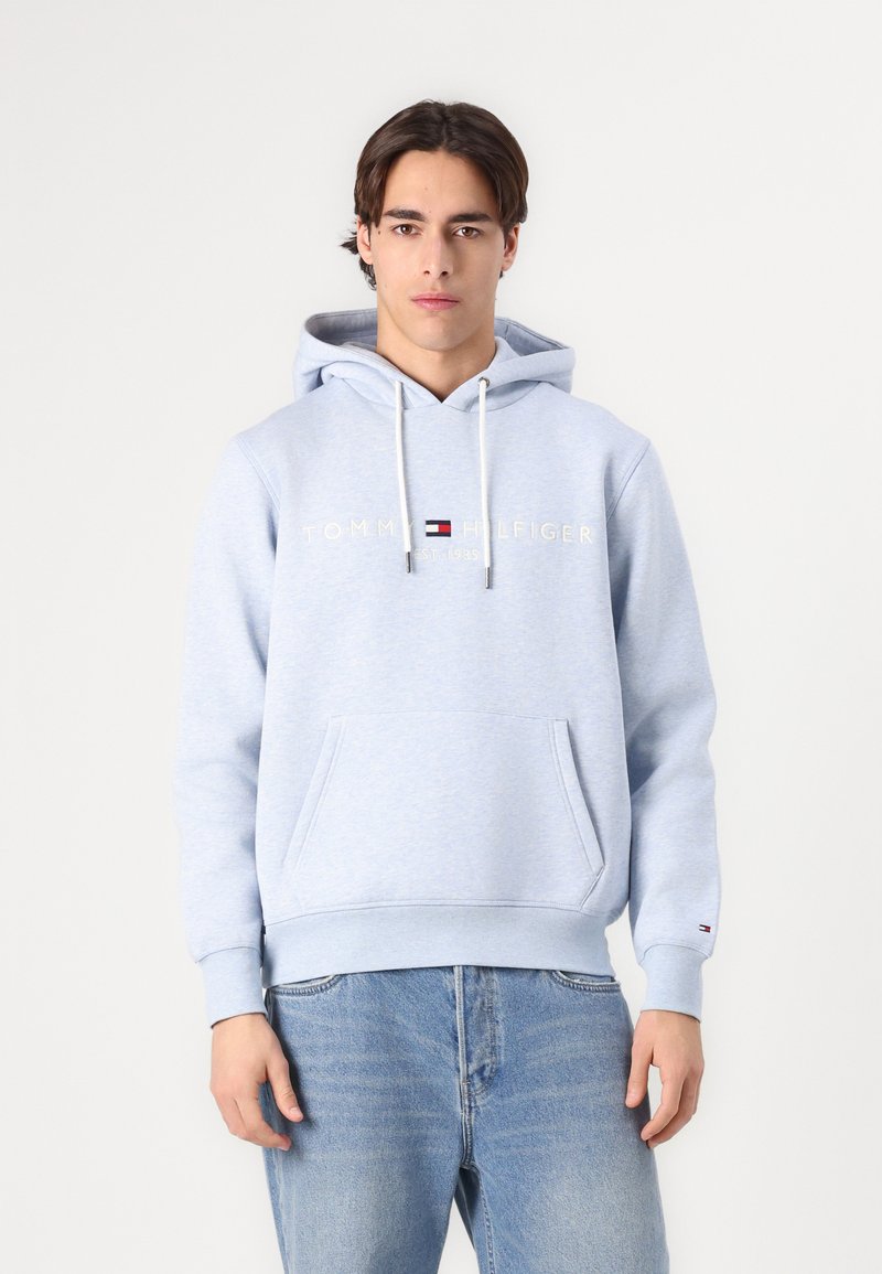 Svijetloplava dukserica s kenguruh džepom, bijelim špagama i "TOMMY HILFIGER" logotipom u zlatnoj boji iznad grudnog koša. Mekana tekstura tkanine.