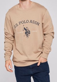 Khakifärgad sweatshirt med rund hals och långa ärmar, med ett marinblått motiv av polospelare och texten "U.S. POLO ASSN. SINCE 1890."