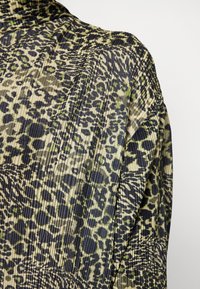 Vêtement à manches longues en tissu léger plissé, présentant un motif léopard vert et noir avec une texture côtelée.