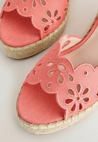 Sandales espadrilles tissées roses à bout ouvert avec motifs floraux découpés et semelles en jute tressée sur fond clair.