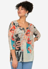 T-shirt à manches longues en crème clair avec des imprimés abstraits de lèvres et du texte en rouge, noir et bleu. Matière douce avec une coupe décontractée.