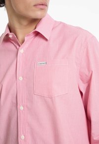 Piros és fehér csíkos ing, mellzsebében "Guess Jeans" címkével; könnyű anyagból készült.