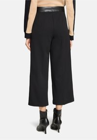 Czarne spodnie o szerokich nogawkach z gładką teksturą, z skórzanym paskiem. Nogawki mają czyste wykończenie i luźny krój.
