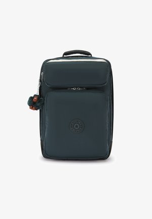 Donkerblauwe stof rugzak met bovenhandvat, voorzak met rits, logo-patch en een kleine harige aap sleutelhanger eraan bevestigd.