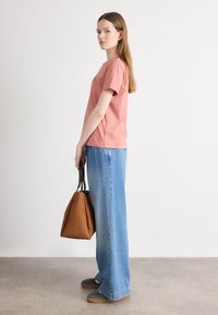 Rosenfarget bomulls t-skjorte kombinert med vide blå denimjeans. Svart og brun håndveske, grå joggesko med brune såler, minimalistisk stil.